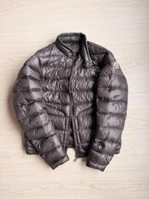 Mörkgrå dunjacka från Moncler - Säljer en mörkgrå dunjacka från Moncler i model Acorus med klassisk quiltad design och hög krage. Jackan har små hål vid handlederna och så är även ena dragkedjan sönder men alla delar fås med för att laga den därav det billiga priset. Storlek 2 som motsvarar M. Hör av er vid frågor!
