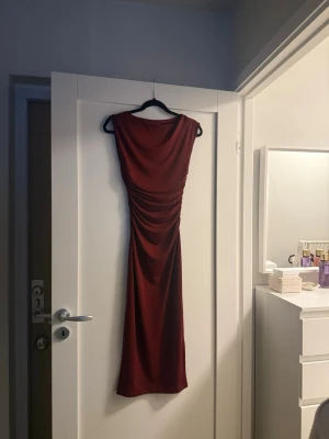 Vinröd långklänning med rynk - Säljer en vinröd långklänning med rynkade detaljer längs sidorna. Väldigt fin passform, endast använt en gång.