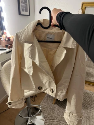 Beige trenchcoat  - Säljer min Snygga croppade trenchcoat i beige, stora dekorativa knappar och detaljer. Super fin att ha nu till hösten 