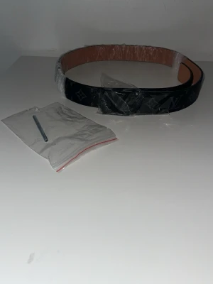  Louis Vuitto - Stilrent svart bälte från Louis Vuitto med klassiskt monogrammönster och insida i ljusbrunt läder. Perfekt accessoar för att lyfta din outfit med en lyxig touch. Levereras med tillbehör som syns på bilden.