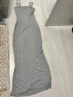 Grå lång klänning H&M - Lång grå klänning från H&M. Klänningen har smala axelband och en enkel, figurnära passform som ger en avslappnad men ändå stilren look.