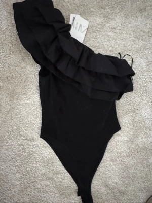 Svart one shoulder body med volang - Snygg svart body från zara, aldrig använd prislapp kvar☺️Passar mig som vanligtvis bär s