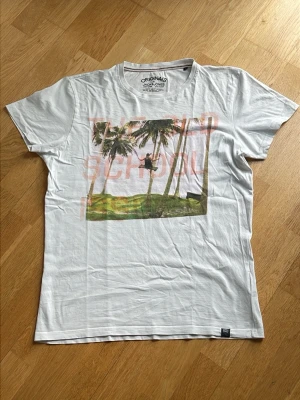 Vit t-shirt med palmtryck Jack & Jones - Vit t-shirt från Jack & Jones med tryck av palmer och text på framsidan. Klassisk rund halsringning och korta ärmar. Perfekt för en avslappnad stil.