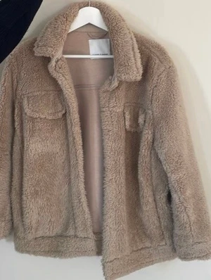 Teddyjacka - Mysig teddyjacka i beige från Samsøe Samsøe. Jackan har klassisk krage, två bröstfickor som stängs med knappar och två sidofickor.