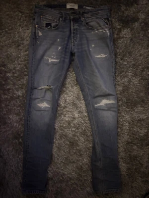 Replay jeans  - Snygga blå skinny jeans från Replay med slitningar och hål på benen för en trendig look. Jeansen har klassisk femficksdesign, knappgylf och ljus tvätt. Perfekta för dig som gillar en avslappnad och modern stil.