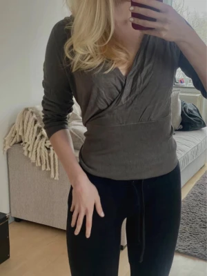 Mörkgrå omlottopp med långa ärmar - Snygg mörkgrå omlottopp med långa ärmar och bred mudd i midjan. Tröjan har en djup v-ringning och är tillverkad i ett mjukt, stretchigt material som sitter skönt på kroppen💕