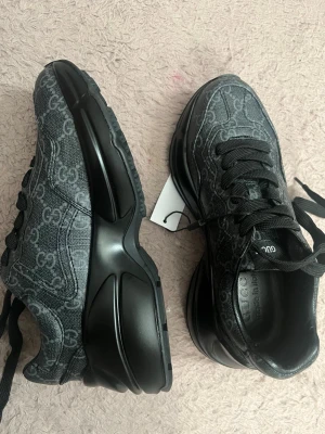 Svarta sneakers från Gucci - Snygga svarta sneakers från Gucci med GG-monogram över hela ovandelen. Skorna har svarta snören, robust svart sula och en modern siluett. Materialet ser ut att vara canvas med detaljer i läder. Perfekta för dig som gillar exklusiv streetstyle.