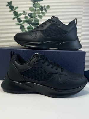 Svarta sneakers från Dior - Snygga svarta sneakers från Dior med diskret mönstrad textilpanel på sidorna och detaljer i slätt läder. Skorna har en chunky sula, svarta skosnören och perforeringar vid tån för extra stil. Perfekta för dig som gillar en clean och modern look.