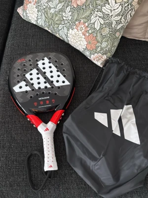 Adidas padelracket Metalbone - HELT NYTT!!!Säljer ett Adidas padelracket Metalbone i svart och rött med vitt grepp och stora vita detaljer på träffytan. Racketet har många hål och kommer med en svart dragskopåse med Adidas-logga. Perfekt för dig som vill ta ditt padelspel till nästa nivå. 