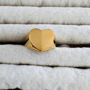 Paket pris  - Säljer två snygga ringar i guldfärg. Den ena ringen har en stor hjärtformad front och den andra är öppen med två detaljerade vingar. Båda ringarna har en modern och trendig design som sticker ut. Perfekta accessoarer för att lyfta din stil.