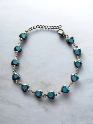 Silverarmband med blå hjärtan - Ett stilrent armband i silverfärg med små blå hjärtformade stenar längs hela kedjan. Justerbar längd med karbinlås. Perfekt accessoar för att addera lite färg till din look.