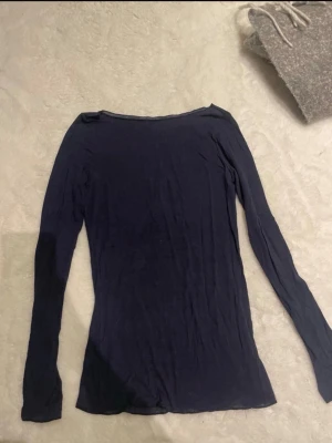Mörkblå långärmad topp - En enkel och stilren mörkblå långärmad topp med rund halsringning. Toppen har en tight passform och är tillverkad i ett mjukt material som känns skönt mot huden. Perfekt att matcha med jeans eller kjol.