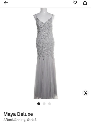 Balklänning  - Lång, figurnära aftonklänning från Maya Deluxe i silver med smala axelband. Överdelen är täckt av glittrande paljetter och pärlor, medan kjolen är i flera lager av tunn tyll. Perfekt för dig som vill sticka ut på bal eller gala.