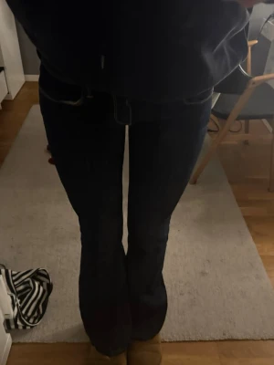 Mörkblå bootcut jeans - Säljer ett par mörkblå bootcut jeans med klassisk femficksdesign och låg midja. Jeansen har en snygg passform som sitter tajt över låren och släpper ut vid vaden. Perfekta för dig som gillar en tidlös och stilren look.