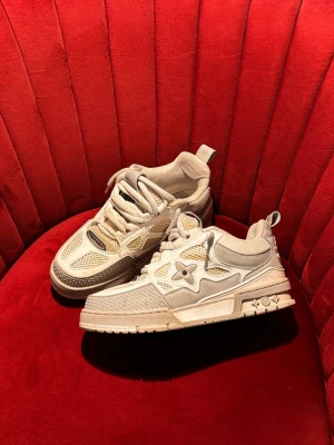 Louis Vuitton Skates vita sneakers - Säljer ett par vita Louis Vuitton sneakers med mesh och läderdetaljer. Skorna har en chunky sula, LV-logga på sidan och coola detaljer på hälen. Perfekta för dig som gillar streetwear och exklusiva märken.