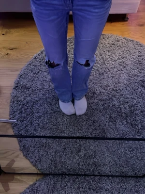 Blå jeans med hål - Säljer ett par ljusblå bootcut jeans  och slitna hål på båda knäna.  