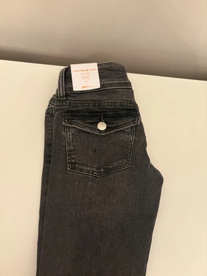 Grå flare jeans från Gina Tricot - Snygga gråa flare jeans från Gina Tricot med klassisk femficksmodell och knappdetalj på bakfickan. Jeansen har en trendig utsvängd passform och är tillverkade i mjukt denimtyg. Perfekta för dig som vill ha en cool och avslappnad stil.