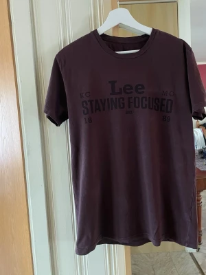 Mörkbrun Lee t-shirt med tryck - Snygg mörkbrun t-shirt från Lee med svart texttryck 'Staying Focused' på bröstet. Klassisk rund halsringning och korta ärmar. Perfekt för en avslappnad och cool stil. Stl L - slim fit. Herr storlek. 