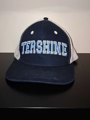 Blå och vit Tershine keps - Snygg blå keps från Tershine med vit mesh på sidorna och bak. Framtill står det 'TERSHINE' i stora bokstäver med ljusblå och vita detaljer. Klassisk böjd skärm och justerbar baksida. Perfekt för en avslappnad streetwear-look. Priset är ej hugget i sten.