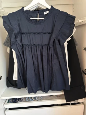 Mörkblå volangblus från meat me there  - Söt mörkblå blus från meat me there med volangärmar och dekorativa broderidetaljer framtill. Blusen har rund halsringning och ett lätt, luftigt tyg 