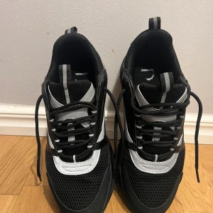 Svarta chunky sneakers med vita detaljer - Snygga svarta sneakers med chunky sula och vita samt grå detaljer. Ovandelen är i mesh och syntetmaterial för en sportig look. Perfekta för dig som gillar streetstyle och vill ha bekväma skor till vardags.