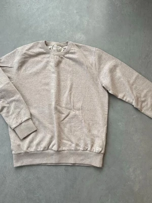 Beige sweatshirt från Crossley - Snygg beige sweatshirt från Crossley i 100% hållbart material. Tröjan har rund hals, ribbade muddar vid ärmslut och nederkant samt en avslappnad passform. Perfekt för en chill och stilren look. Haft i några år. Bra skick. Tröjan är storlek XL men jag tycker den passar mer som en storlek L. 