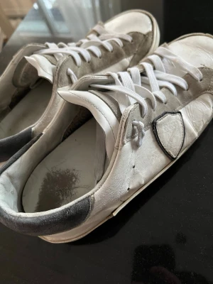 Vita och grå sneakers från Philippe Model - Snygga vita och grå sneakers från Philippe Model med klassisk låg siluett. Skorna har slitningar i hälen på sulorna.priset är inte hugget i sten.