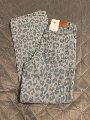Ljusblå leopardmönstrade jeans STAY - Säljer ett par ljusblå jeans från STAY med snyggt leopardmönster i blå toner. Klassisk femficksmodell med raka ben och hög midja. Jeansen är gjorda i denim och har en cool, trendig vibe som sticker ut i mängden.
