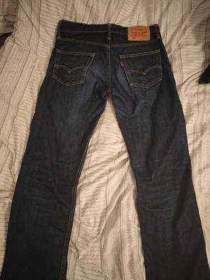 Levi's 504 mörkblå jeans - Säljer ett par klassiska Levi's 504 jeans i mörkblå denim med raka ben och snygga kontrastsömmar. Jeansen har två bakfickor med den ikoniska V-formade sömmen och läderpatch bak i midjan. Perfekta för en avslappnad och stilren look. DÅLIG KVALITE PÅ BILDER!