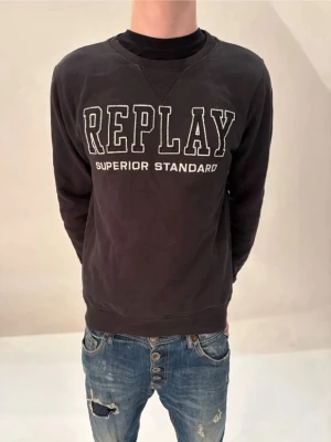 Svart sweatshirt från Replay - Cool svart sweatshirt från Replay med stor vit logga och texten 'Superior Standard' på bröstet. Klassisk rund halsringning och mjukt material som känns skönt mot huden. Perfekt till jeans för en avslappnad look.