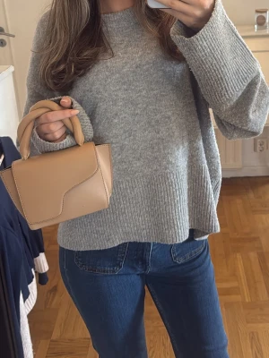 Grå oversized stickad tröja - Mysig grå stickad tröja i oversized modell med breda ärmar och ribbade muddar. Tröjan har rund halsringning och är perfekt för lager på lager. Passar till jeans eller kjol för en avslappnad look.