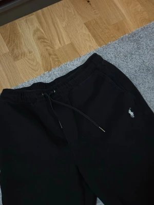 Svarta mjukisbyxor från Polo Ralph Lauren - Säljer ett par svarta mjukisbyxor från Polo Ralph Lauren i storlek S. Byxorna har en broderad vit logga på vänster sida och är tillverkade i mjukt bomullsmaterial. Perfekta för chill dagar eller när du vill vara bekväm.