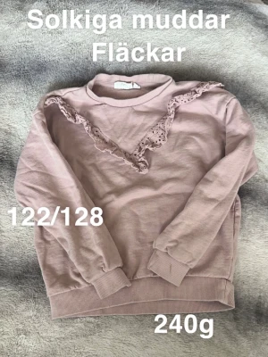 Rosa sweatshirt med spetsdetalj - Söt rosa sweatshirt med rund hals och dekorativ spets i V-form framtill. Tröjan har ribbade muddar vid ärmslut och nederkant samt en avslappnad passform. Perfekt för en casual och trendig look.🌸 Solkiga muddar. Fläckar. Storlek 122/128