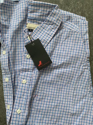 Blårutig skjorta från J. Lindeberg - Klassisk blårutig skjorta från J. Lindeberg med vita knappar och krage. Skjortan har ett stilrent rutmönster i blått, vitt och rött och är tillverkad i mjuk bomull. Perfekt för en clean och avslappnad look.