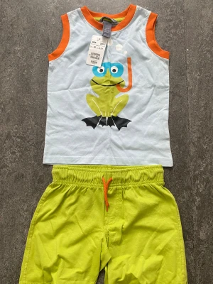 Limegröna shorts från H&M barn - Säljer ett par limegröna shorts från H&M med resårmidja och dragsko i orange. Shortsen är gjorda i mjuk bomull och har en avslappnad passform, perfekta för varma dagar.