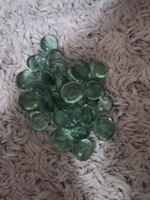Gröna dekorationsstenar i glas - Ett gäng runda, platta dekorationsstenar i genomskinligt grönt glas. Perfekta för pyssel, dekorationer eller att använda i blomkrukor och vaser. Ger ett snyggt och stilrent intryck och kan användas på många kreativa sätt.