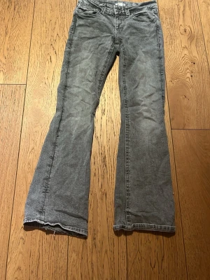 Grå bootcut jeans med låg midja - Säljer ett par grå bootcut jeans med låg midja och klassiska fem fickor. Jeansen har en avslappnad passform och är tillverkade i mjukt denimtyg. Perfekta för en chill och trendig look. Lite slita längst ner se bild.