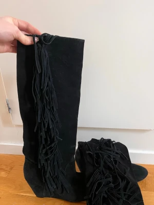 Svarta mockastövlar med fransar - Snygga svarta stövlar i mocka med kilklack och långa fransar längs utsidan. Passar någon med storlek 39/40. Köparen står för frakten💕