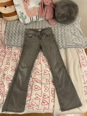 Gina tricot grå bootcut jeans med låg midja - Säljer ett par grå bootcut jeans från Gina med låg midja, utsvängda ben och detaljerade bakfickor. Lite slitna längst ner men inga fläckar eller större hål någonstans. 