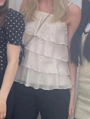 Ljusrosa volanglinne med prickar - Säljer ett ljusbeige linne med tunna axelband och flera lager volanger. Tyget har små diskreta prickar som ger en söt och trendig look. Perfekt för dig som gillar en luftig och feminin stil.