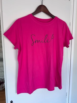 Rosa t-shirt med tryck, storlek L - Försvinner den 31:a mars om den inte sålts innan dess :) Snygg rosa t-shirt med svart texten 'Smile'. Perfekt färgklick! Använd ett par gånger.