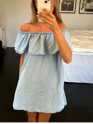 Ljusblå offshoulder klänning - Söt ljusblå kortklänning i offshoulder-modell med volang upptill. Klänningen har en avslappnad passform och är tillverkad i ett mjukt bomullsliknande material. Perfekt för varma dagar och ger en fräsch sommarkänsla.