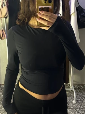 Svart långärmad croppad topp - En svart, långärmad och croppad topp med tight passform. Toppen har en enkel och stilren design utan synliga detaljer eller mönster, perfekt att matcha med olika outfits. Materialet ser ut att vara stretchigt och bekvämt.