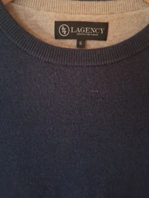 Mörkblå stickad tröja från Lagency - En stilren mörkblå stickad tröja från Lagency i storlek S. Tröjan har rund halsringning, ribbade muddar vid ärmslut och nederkant samt långärmad passform. Perfekt för dig som gillar enkel och klassisk design med en snygg färg.