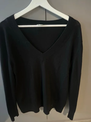 Svart V-ringad stickad tröja  - Svart stickad tröja med V-ringning och långa ärmar. Tillverkad i merino ull.