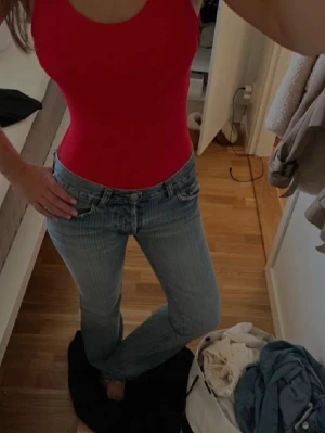 Röd body med djup rygg - Snygg röd body med breda axelband och rundad halsringning framtill. Baksidan har en djup urringning som ger en trendig look. Tight passform som framhäver figuren. Perfekt att styla med jeans eller kjol. Materialet ser stretchigt och bekvämt ut.