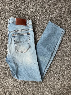 Ljusblå  jeans från Tiger of Sweden - Säljer ett par ljusblå jeans från Tiger of Sweden. Jeansen har klassisk femficksdesign, läderpatch bak i midjan och är tillverkade i stretchig denim för en bekväm passform. Perfekta för en avslappnad och trendig look.