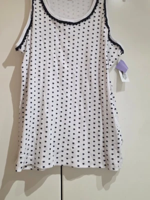 Vit ribbad linnetopp från Miss Milla - Säljer en vit ribbad linnetopp från Miss Milla med små marinblåa stjärnor över hela tyget. Toppen har marimblåa detaljer vid halsringningen och ärmlösa kanter. Perfekt för chill dagar hemma eller som ett lager under en hoodie.