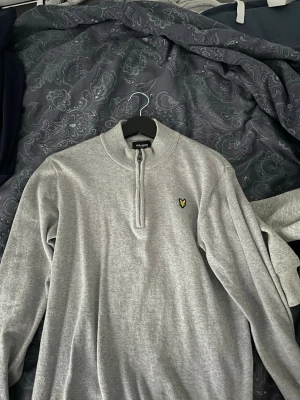 Grå half zip tröja från Lyle & Scott - Säljer för den passa inte mig helt ny Snygg grå tröja från Lyle & Scott med half zip och klassisk gul logga på bröstet. Tröjan har hög krage och är tillverkad i mjuk bomullsmix, perfekt för en stilren och avslappnad look.