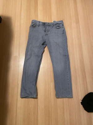 Jack n Jones ljusgrå jeans, storlek 32/32 - Klassiska Jack n jones jeans i en ljusgrå tvätt. Rak passform med knappgylf och femficksdesign. Perfekta för dig som gillar en tidlös och avslappnad stil. Tillverkade i slitstarkt jeanstyg.
